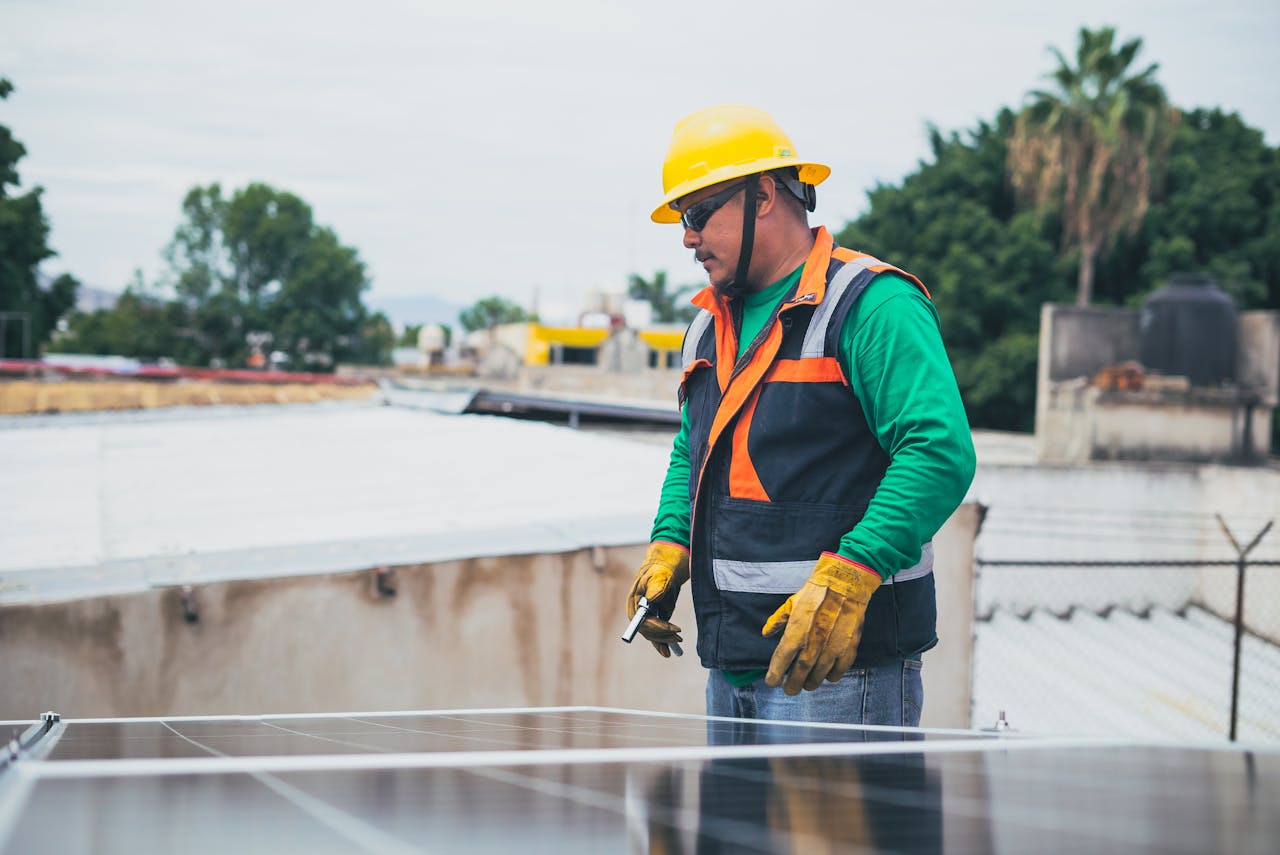 A solar technician in protective gear inspecting rooftop solar panels outdoors.